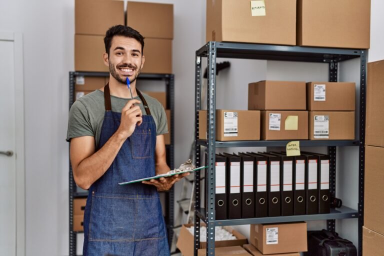 Young hispanic man business worker writing on clipboard at storehouse